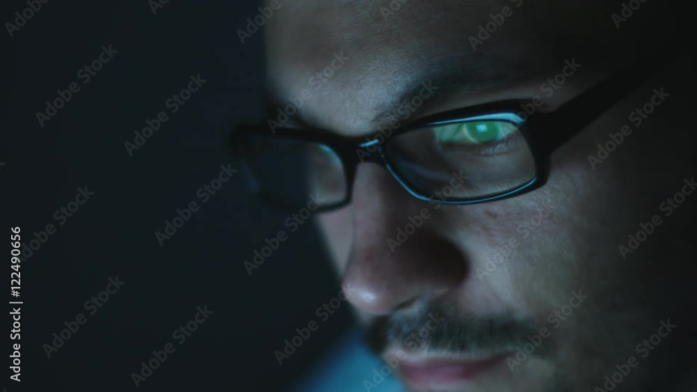 Side view of young man with glass work on laptop in the dark. Close-up shot Side view of young man with glass work on laptop in the dark. Close-up shot