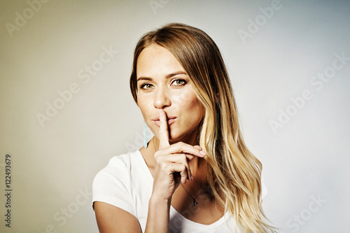 Fotografie Closeup portrait secretive young woman placing finger on lips as