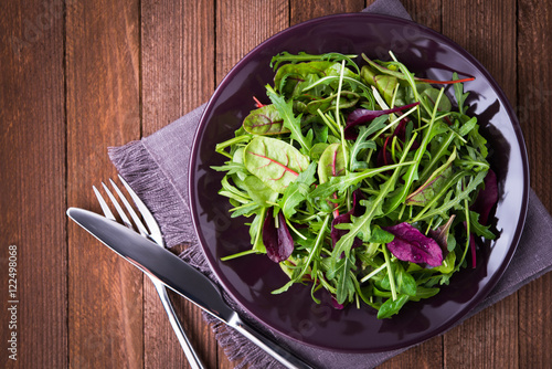 Fresh salad with mixed greens  arugula  mesclun  mache  on dark wooden background top view. Healthy food.