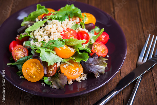 Fresh healthy salad with quinoa, cherry tomatoes and mixed greens (arugula, mesclun, mache) on wood background close up. Food and health. Superfood.