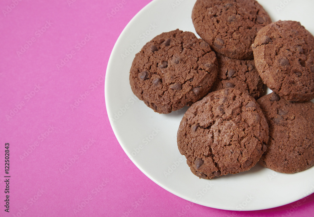 A plate of chocolate chunk cookies on a bright pink background forming a page border A plate of chocolate chunk cookies on a bright pink background forming a page border