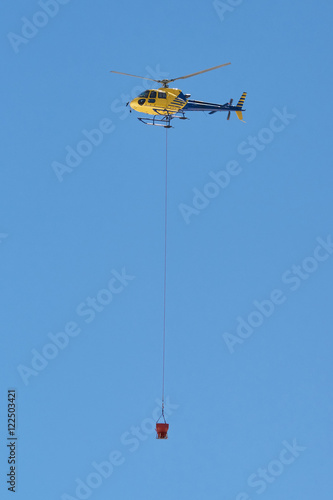 Gelber Hubschrauber transportiert Betonkübel im Baustelleneinsatz