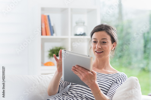  cheerful woman at home using a tablet, she sits on a white sofa