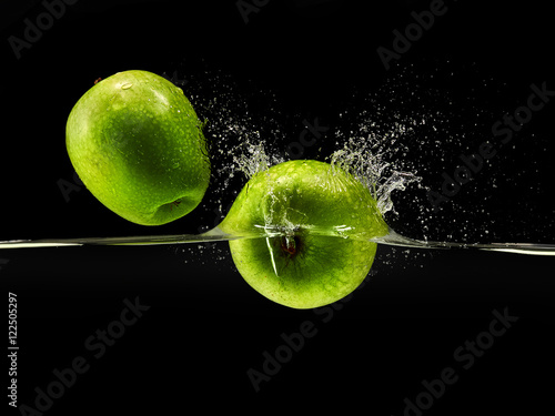 Group of green apples falling in water on black background