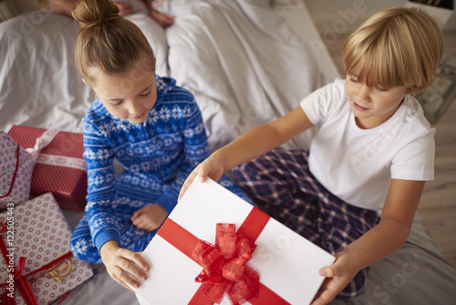 Kids opening big Christmas gift in the bed
