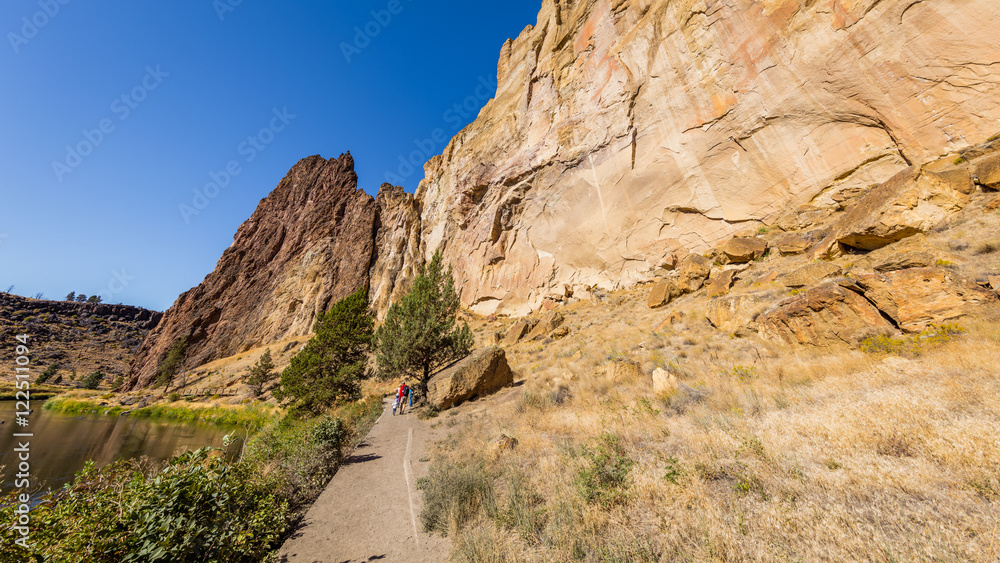 The path between the rock and the river. The river is flowing among the rocks. Colorful Canyon. Amazing landscape of yellow sharp cliffs. Smith Rock state park, Oregon The path between the rock and the river. The river is flowing among the rocks. Colorful Canyon. Amazing landscape of yellow sharp cliffs. Smith Rock state park, Oregon