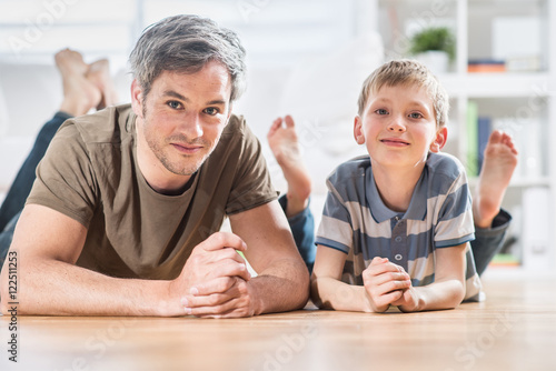 At home, Daddy and his young son are lying on the wooden floor