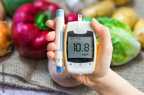 Diabetic diet and diabetes concept. Hand holds glucometer. Vegetables in background. photo