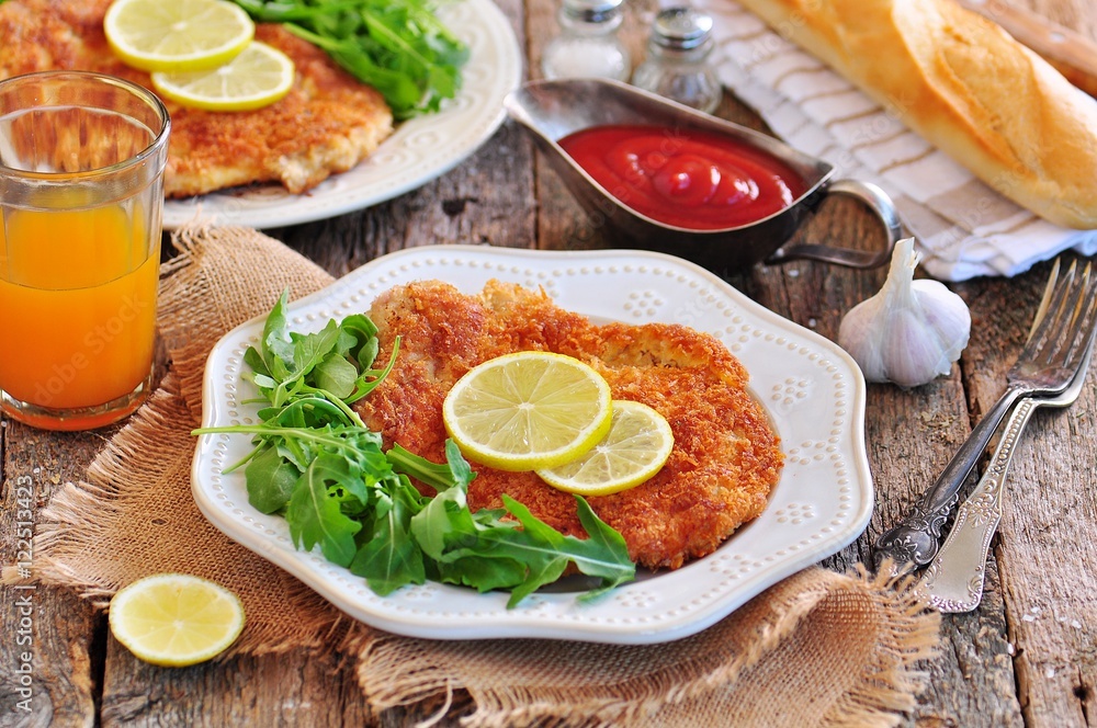 Pork schnitzel with organic arugula and lime on a old wooden background.