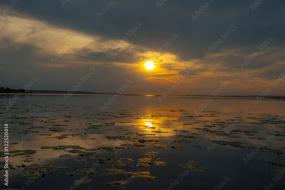 Golden sunset creeps over the clouds and sun reflected in the water surface of the lake