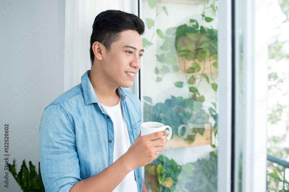 Thoughtful asian man looking out the window in bedroom at home Thoughtful asian man looking out the window in bedroom at home