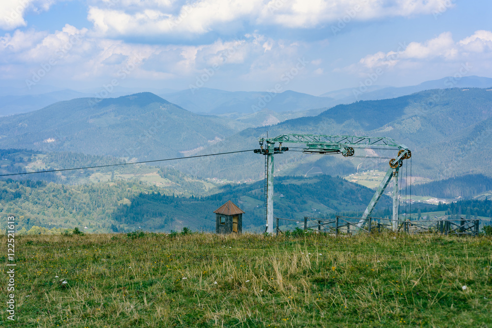 Old rusty lift mechanism in the Carpathians with mountains, fir-trees and beautiful blue sky with clouds in the background. Summer time