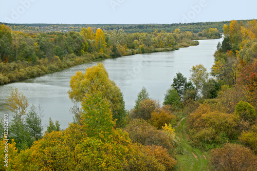 along the river stretches a beautiful autumn forest with gold and green leaves