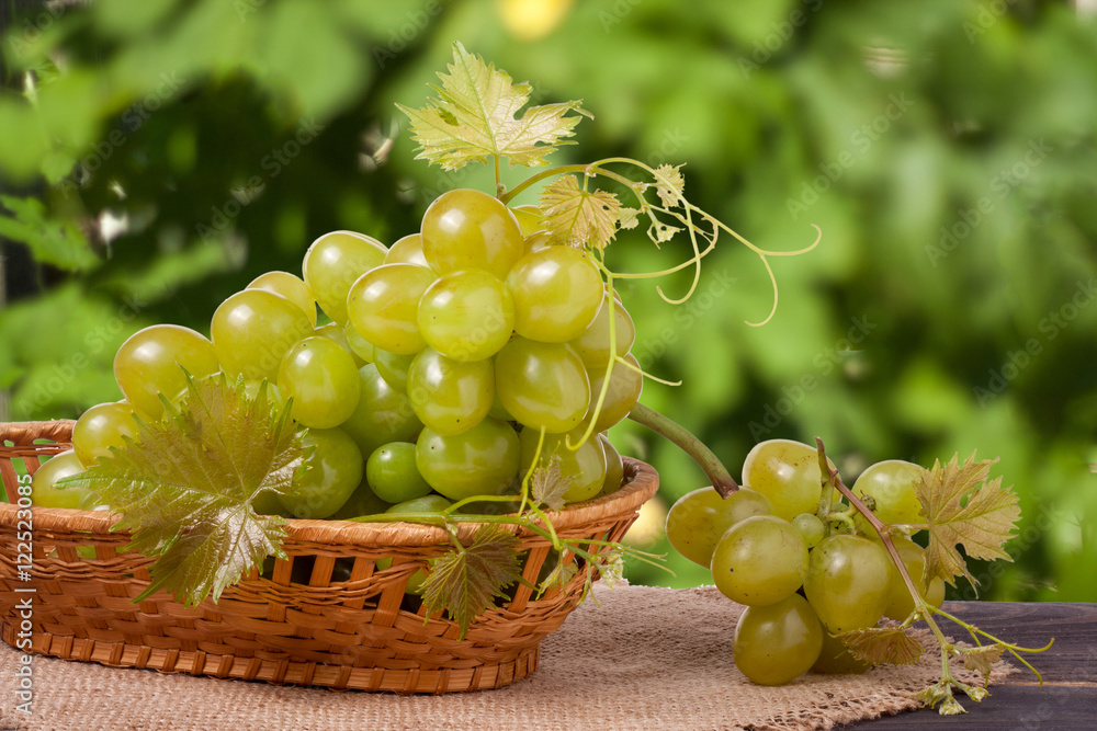 green grapes in a wicker basket on wooden table with blurred background green grapes in a wicker basket on wooden table with blurred background