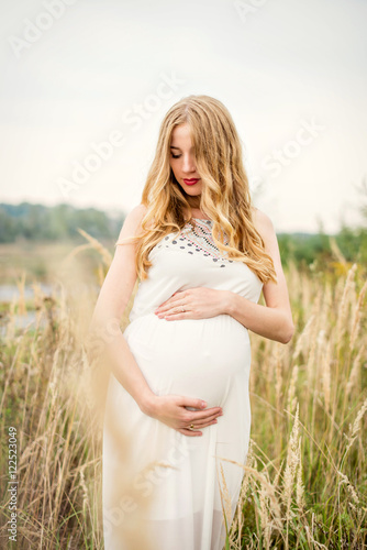 Portrait of a young beautiful pregnant woman with long blond hair in a white dress