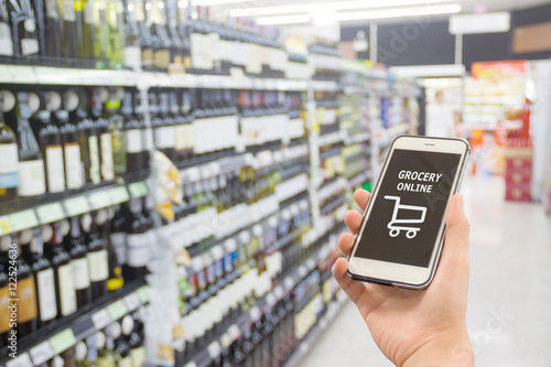 Smart phone with grocery shopping online on screen over blur supermarket background, retail business and technology concept