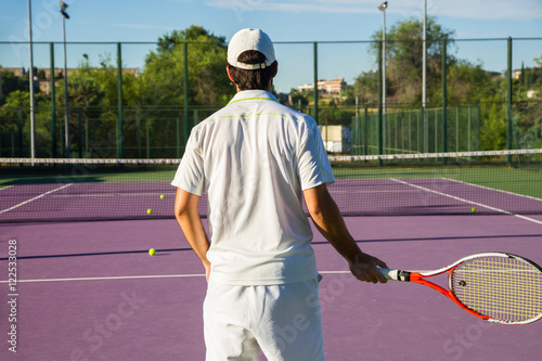Professional tennis player playing the game on the tennis court. He has his back to the camera and have the racket in his right hand. He is in the center of the image. 