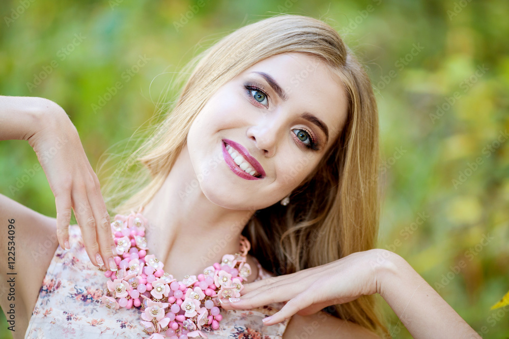Naklejka premium Fashionable stylish young woman with long thick hair in a pink dress and jewelry on the neck on the nature autumn day