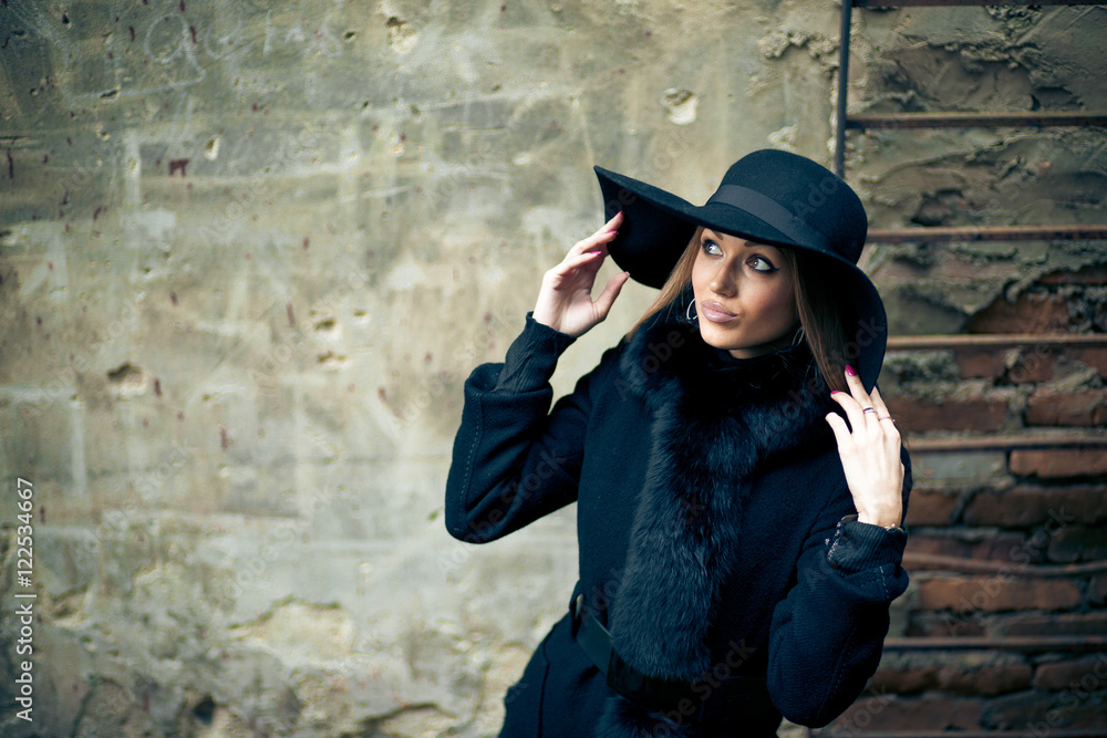 Woman touches her black hat while posing in winter coat Woman touches her black hat while posing in winter coat