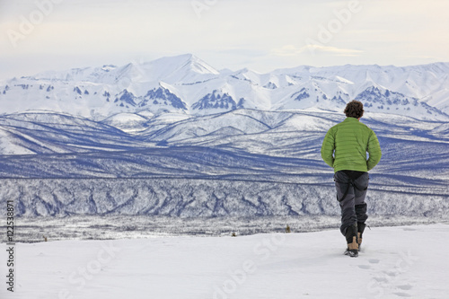 Person walking towards the edge of snow with the Ogilvie Mountains in the distance, Dempster Highway, Yukon Territory, Canada. photo