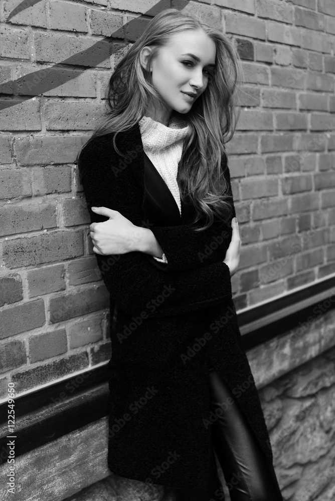 Black and white photo. Beautiful young blonde woman walking on the street. Dressed in a black coat and a warm knit sweater. Black and white photo. Beautiful young blonde woman walking on the street. Dressed in a black coat and a warm knit sweater.