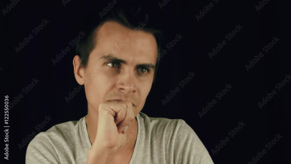 Young men in white t-shirt siting on black background hold fist in front of his mouth Young men in white t-shirt siting on black background hold fist in front of his mouth