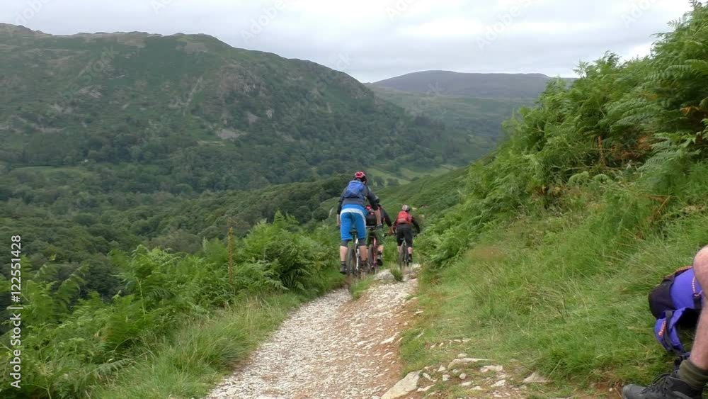 Group of three mountain bicycle riders riding down the trail in Lake District, England. Group of three mountain bicycle riders riding down the trail in Lake District, England.