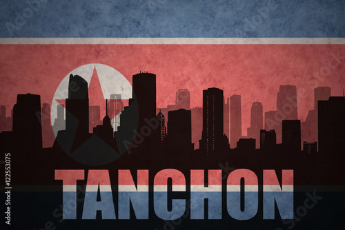 abstract silhouette of the city with text Tanchon at the vintage north korea flag background