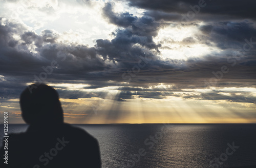 Clouds blue sky and sunlight sunset on horizon ocean Northern Spain Basque Country. Outline looking travel hipster on background seascape dramatic rays sunrise. Relax view waves sea