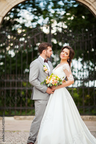 Handsome groom hugging beautiful bride with bouquet in romantic european park