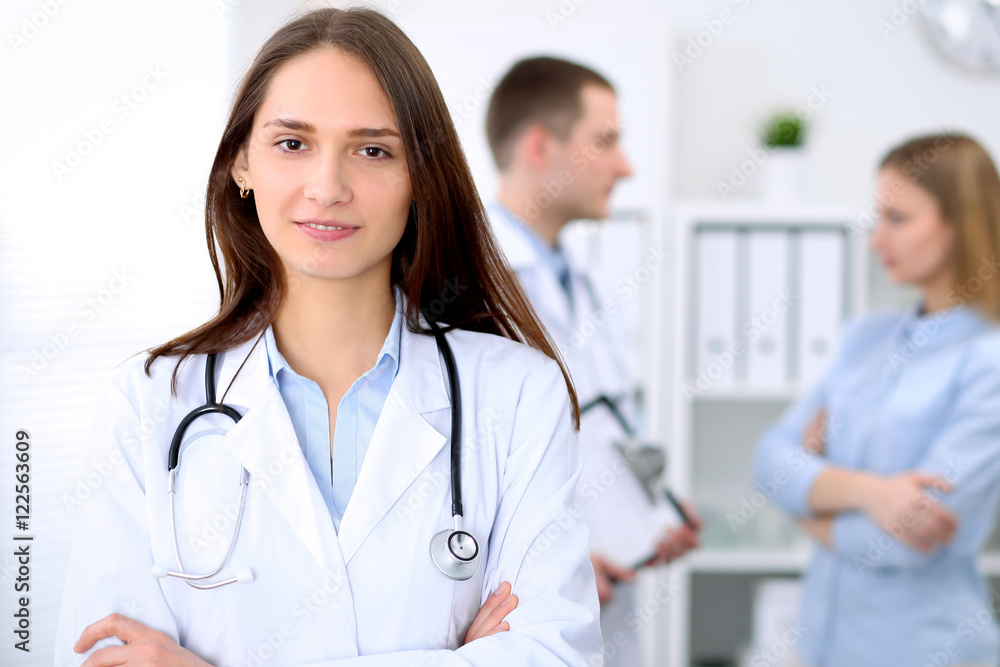 Young beautiful female doctor smiling on the background with patient in hospital. High level and quality medical service concept. Young beautiful female doctor smiling on the background with patient in hospital. High level and quality medical service concept.