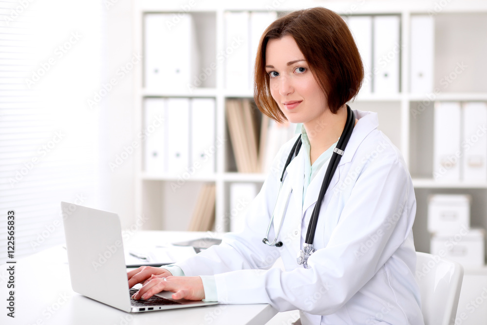 Young brunette female doctor sitting at the table and working at hospital office. Health care, insurance and help concept. Physician ready to examine patient Young brunette female doctor sitting at the table and working at hospital office. Health care, insurance and help concept. Physician ready to examine patient