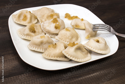 Traditional polish dumplings, "pierogi ruskie" on white plate on wooden table.