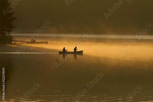 Two men paddle canoe at sunrise on Oxtongue Lake, Muskoka, Ontario, Canada.