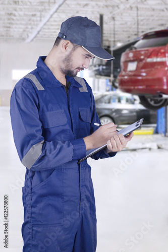 Mechanic writes on clipboard in workshop