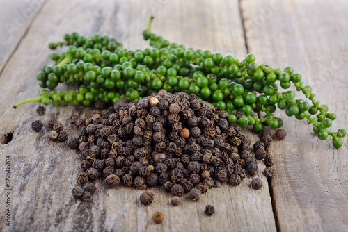 fresh green peppercorns and dry black pepper on wooden table