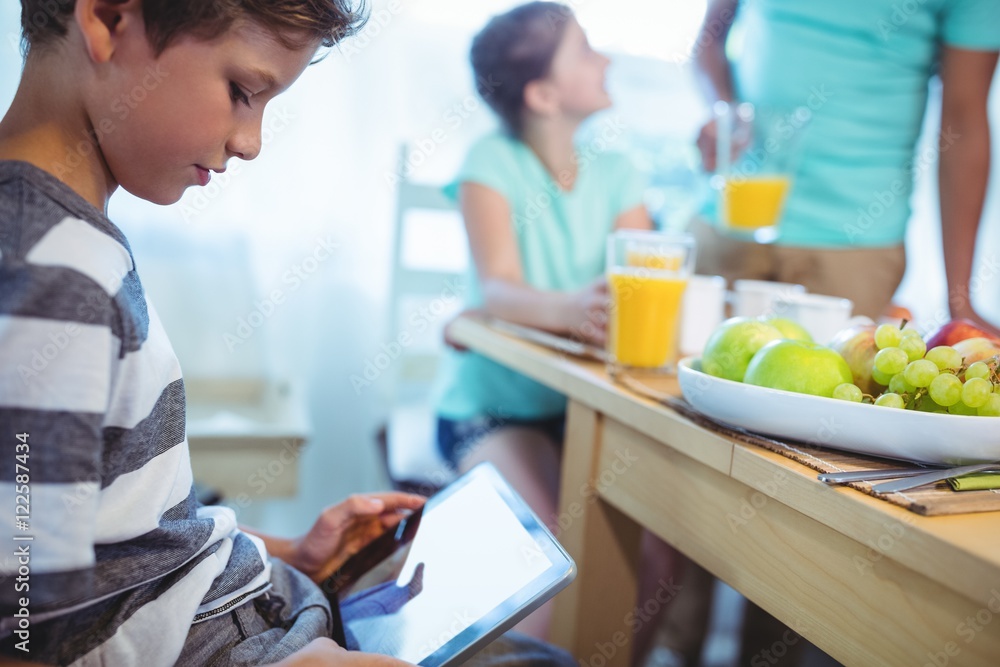 Boy using digital tablet with breakfast on table Boy using digital tablet with breakfast on table
