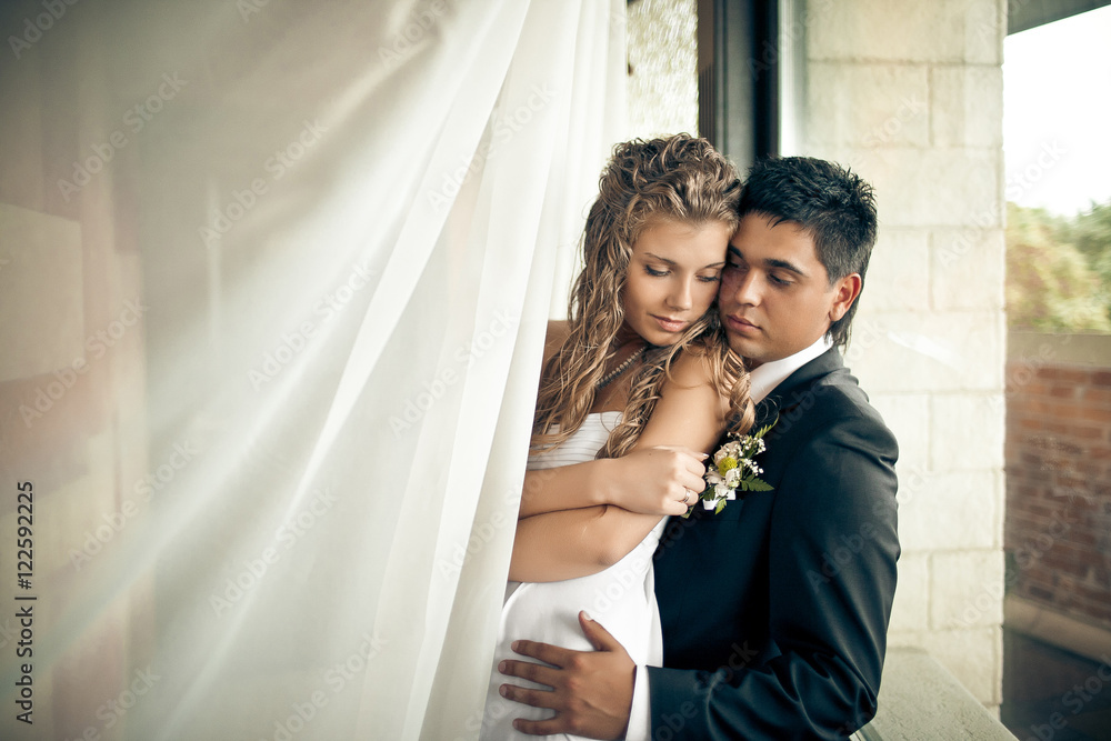 Curly bride hugs her shoulder while leaning to handsome groom Curly bride hugs her shoulder while leaning to handsome groom