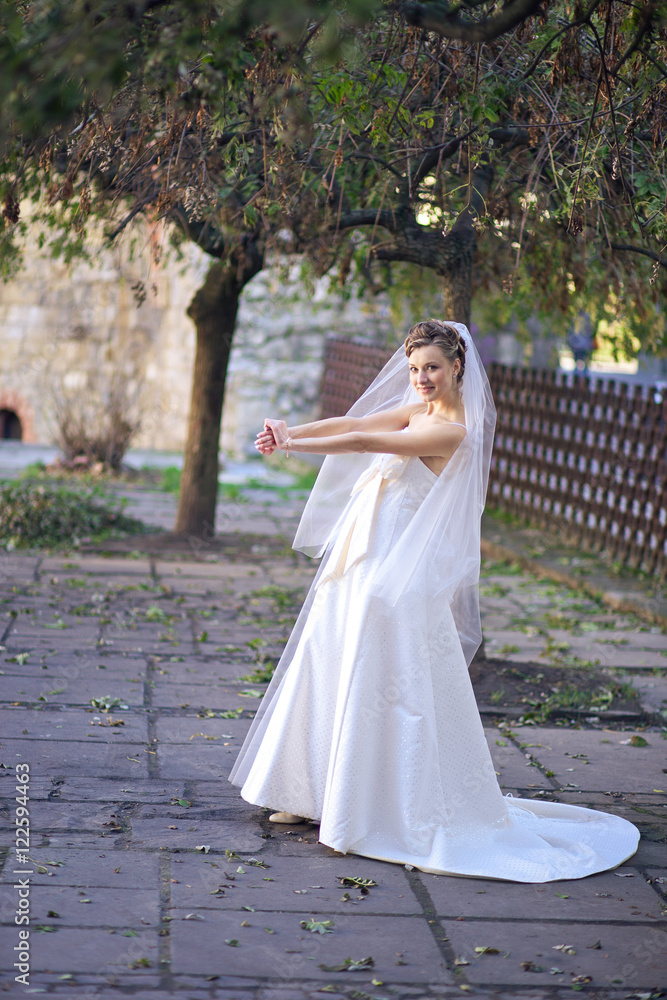 Bride stretches her hands while posing under the green tree Bride stretches her hands while posing under the green tree
