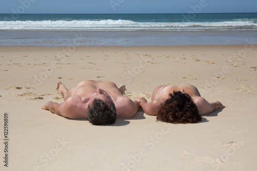 Naturist and loving couple lying on a resort's white sand photo