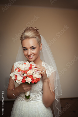Adorable blonde bride holds pretty wedding bouquet while standin