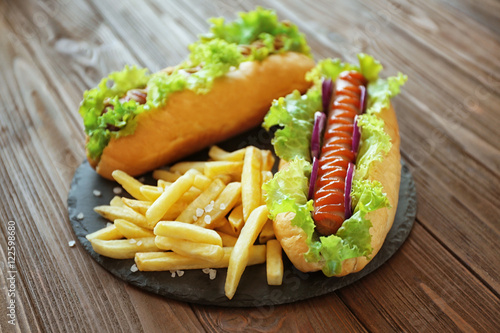 Delicious hot dog and fries on round wooden board