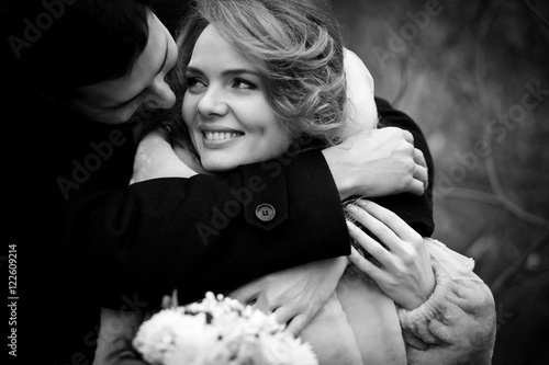 Groom hugs bride from behind hiding her in his broad arms