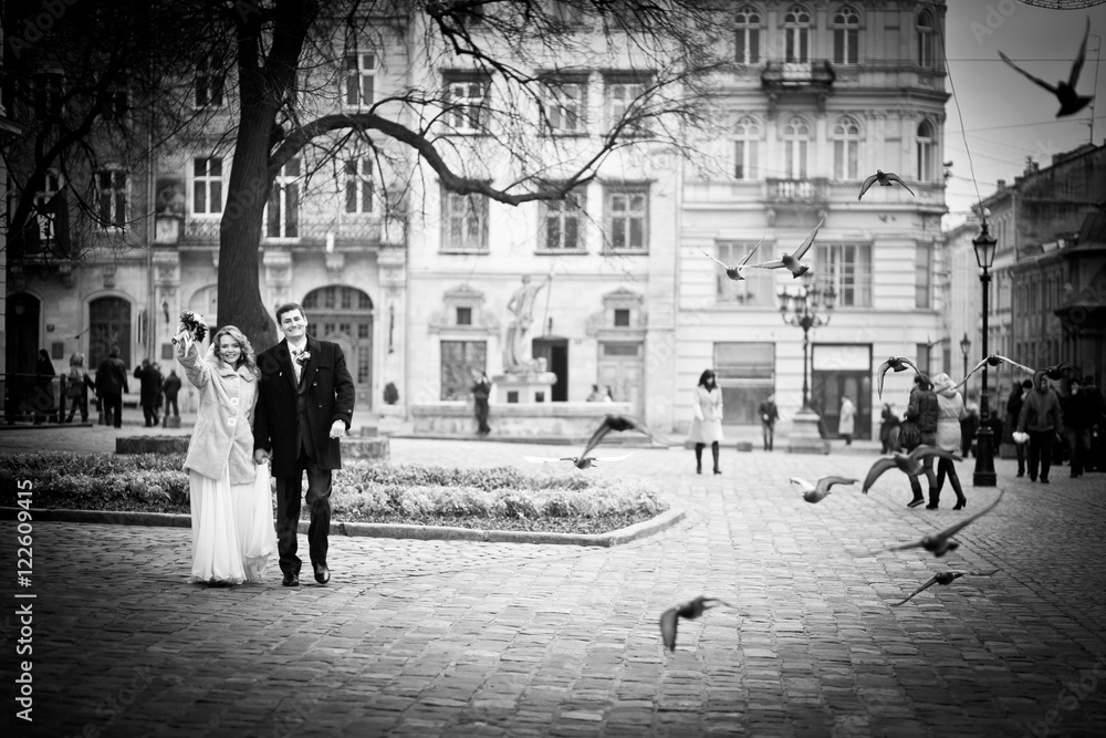 Heavenly wedding couple walks through the square while pigeons f
