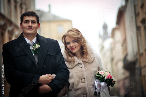 Marvelous bride with soft smile walks with goom around the city photo