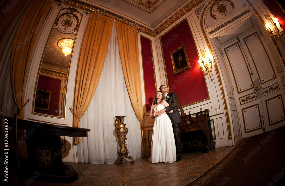 Look from below at proud groom hugging bride from behind in rich