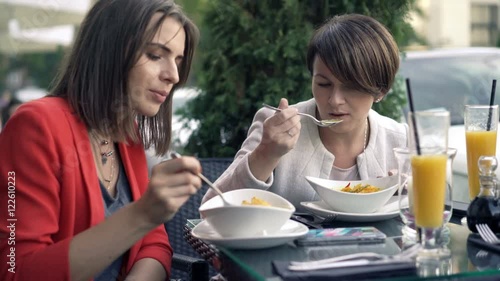 Two pretty girlfriends talking and eating soup in cafe in city
 photo