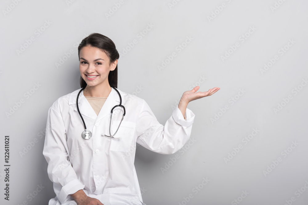 Cheerful professional doctor sitting against grey background Cheerful professional doctor sitting against grey background