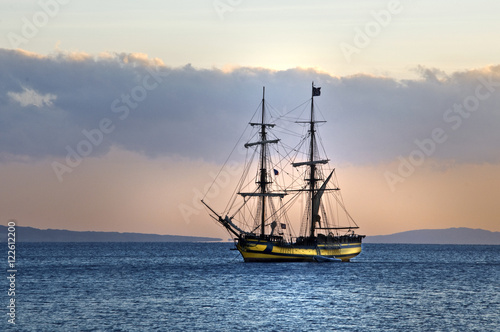 sailing ship at anchor, a blue calm sea and cloudless sky