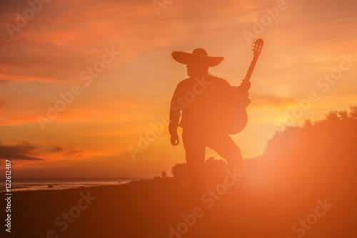 Mexican, Latin American, Spanish. Musician on the coast. Silhouette at sunset.